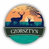 Okrągły magnes na lodówkę z grafiką jelenia na tle zachodzącego słońca.